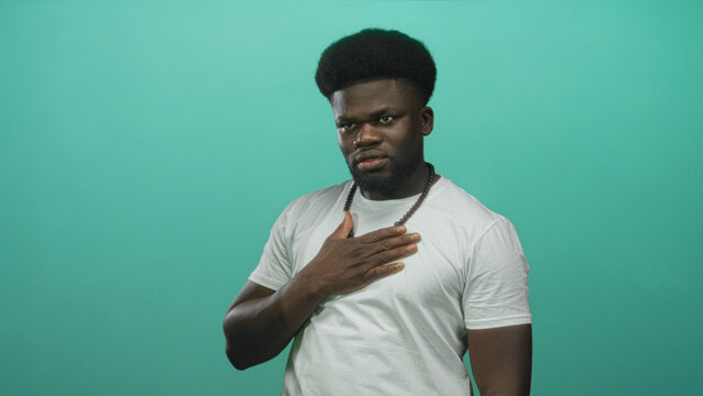 Man with hand on chest and wooden bead necklace in studio, looking solemn with slight frown and raised brows; sincerity apology.