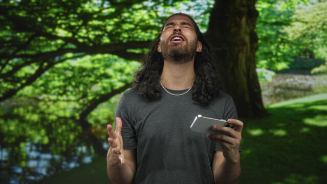 Man holding smartphone singing with mouth open and eyes closed in forest; frustration catharsis release intensity.