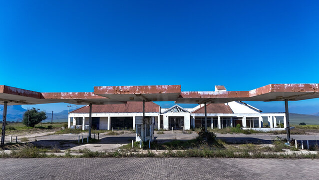 Aerial view of an abandoned gas station with a rusty canopy and white building under a clear blue sky in iNtabazwe, Free State, South Africa.