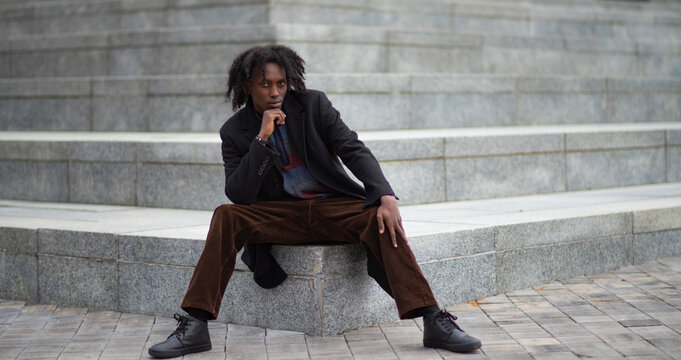 Thoughtful Young Man in Stylish Autumn Outfit Sitting on Stone Steps with Copy Space