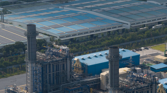 Aerial view of the industrial power plant facility with tall chimneys and large blue-roofed warehouses in the industrial zone of Map Yang Phon, Rayong, Thailand.