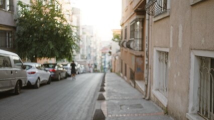 Fototapeta premium Blurred urban street scene with defocused sidewalk and parked cars, soft bokeh on distant buildings street; background copyspace calm.