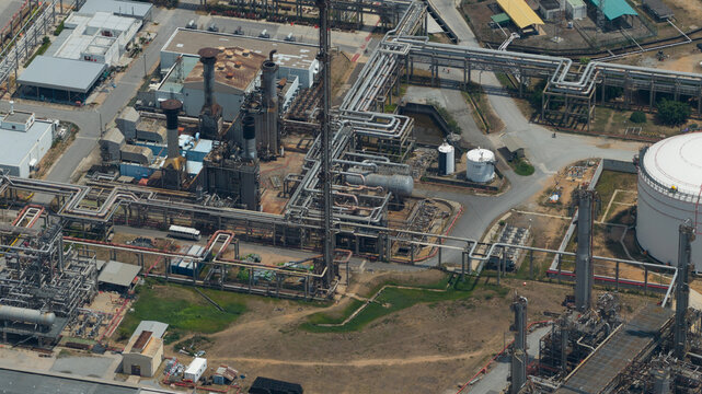 Aerial view of an industrial refinery complex with intricate piping systems, storage tanks, and tall chimneys in Tambon Pa Yup Nai, Chang Wat Rayong, Thailand.