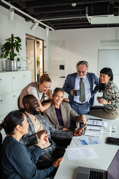 Coworkers laughing over smartphone during team meeting in modern office