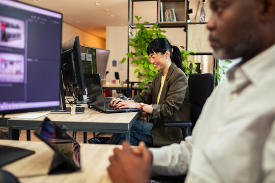 Smiling businesswoman working on laptop in modern open office