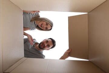 Couple looking into cardboard box on white background, view from inside package © New Africa