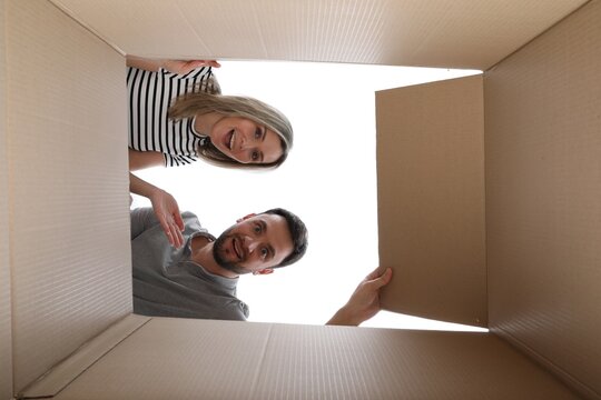 Couple looking into cardboard box on white background, view from inside package