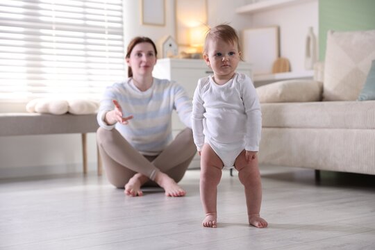 Baby's first steps. Mother supporting daughter while she learning to walk at home, selective focus