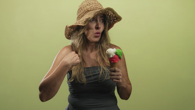 Woman in straw hat holds triple scoop ice cream cone and points to chest in studio; playful summer mood.