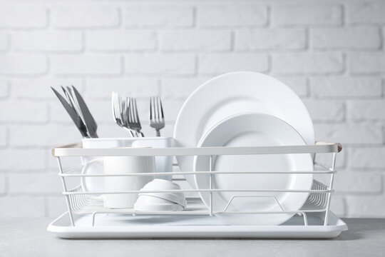 Set of clean dishes and cutlery in drying rack on light grey table, closeup