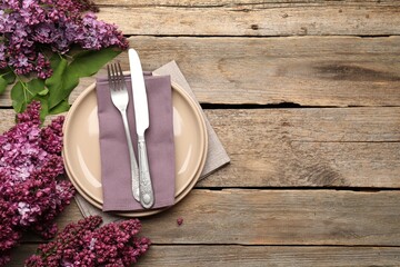 Naklejka premium Stylish setting with plates, cutlery, napkin and flowers on wooden table, flat lay. Space for text