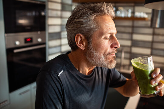 Mature man savoring green smoothie in home kitchen