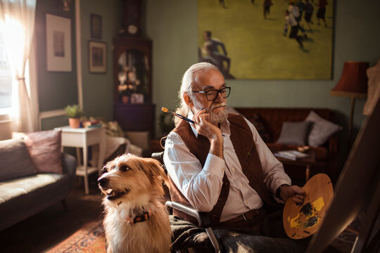 Senior artist in wheelchair painting at home with dog