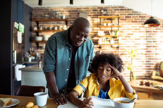 Smiling man helping boy with homework at kitchen table at home