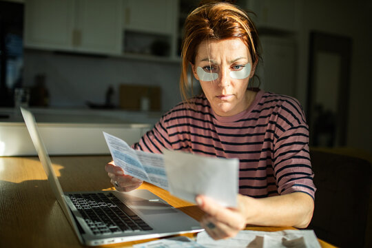 Woman with under eye patches reviewing bills at home