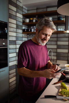 Middle-aged man using smartphone while cooking in a home kitchen