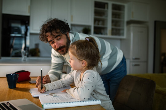 Father helping daughter with homework at kitchen table at home