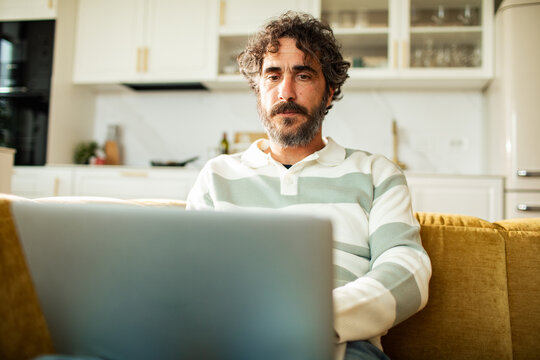 Bearded man working on laptop at home kitchen sofa
