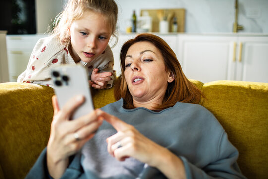 Mother and daughter using smartphone on couch at home