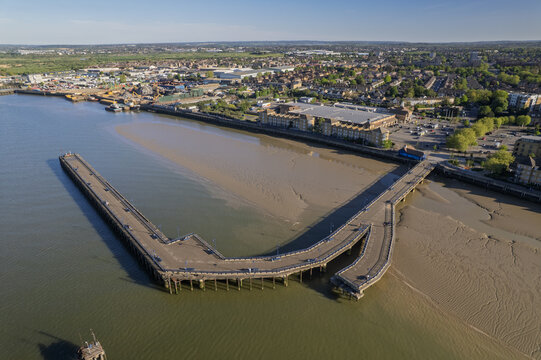 Aerial view of Erith Pier stretching into the River Thames with exposed mudflats at low tide and the surrounding urban landscape in Erith, Greater London, United Kingdom.