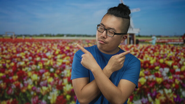 Man pointing both index fingers at opposite directions in a colorful flower field with windmill and blue sky; choice playful.
