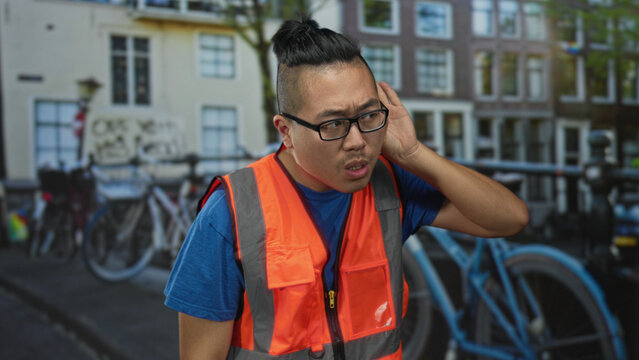 Man in orange reflective vest gives thumbs up on a street in amsterdam beside bicycles and canal buildings; friendly service.