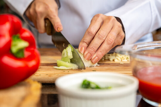Chef cortando cebola fresca com faca sobre t&aacute;bua de madeira em cozinha