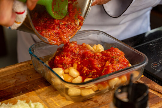 Molho de tomate caseiro sendo despejado sobre nhoque em travessa de vidro na cozinha