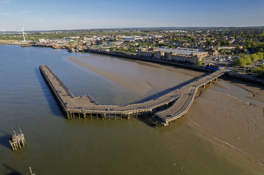 Aerial view of Erith Pier stretching over the River Thames mudflats with people walking and industrial buildings in the background Erith, Greater London, United Kingdom.