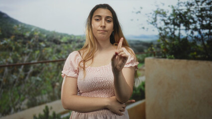 Obraz premium Woman pointing index finger with crossed arms on a building balcony overlooking hills, warning gesture; disapproval.