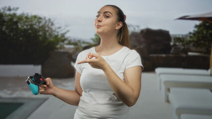 Woman holding gamepad points finger to controller with visible hand beside lounge chairs at building  playful focus. © Krakenimages.com