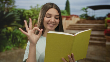 Fototapeta premium Teenage girl reading a green paperback book on stone steps in a park outdoors, holding the book; calm learning concentration.