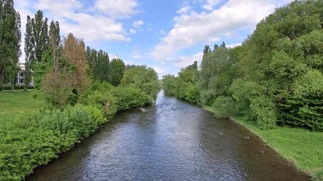 Horizontal 4K slow motion shot of a wide river current surrounded by lush green trees. Captured from a bridge with a static camera at 100 Mbps. Peaceful and cinematic nature scene.