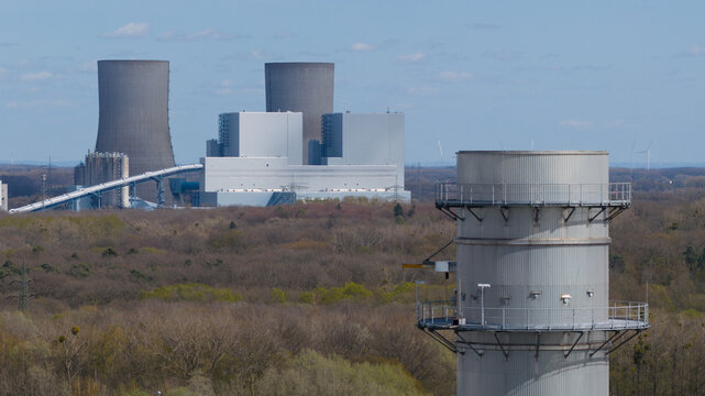 Aerial view of the Trianel Gaskraftwerk Hamm power plant with its cooling towers and industrial buildings surrounded by a dense forest under a clear blue sky Hamm, Nordrhein-Westfalen, Germany.