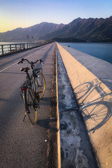 Fototapeta premium Retro bicycle parked on a scenic coastal road with mountains in the background at sunset