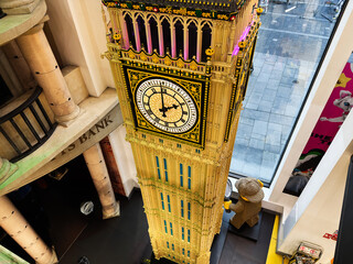 Naklejka premium Interior view of a detailed Big Ben Lego model clock tower display in a London, UK toy store with shoppers and city window backdrop
