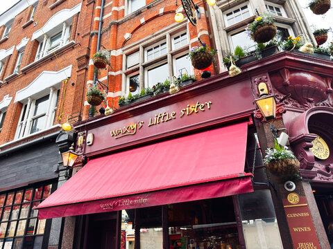 Waxy's Little Sister pub facade with red awning, hanging baskets and Victorian brick architecture in London, UK