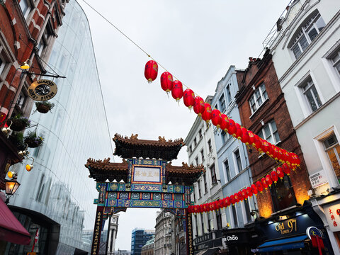 Ornate Chinatown gate with red lanterns strung across a narrow street in London UK, colorful traditional Chinese architecture framed by Victorian and modern buildings during a festive celebration