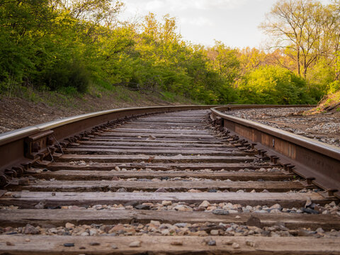 Low angle view of curving railroad tracks with wooden ties and stone ballast winding through a lush green forest in the Chicago suburbs
