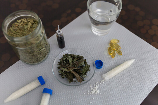 Top view of homeopathic and natural medicine preparations on table: jar of dried herbs, homeopathic pellets in tubes, softgel capsules. Concept of herbal remedies and alternative healthcare.