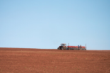 Fototapeta premium Spring sowing campaign. A tractor with a towed seeder is working in the field. Two workers are on the seeder, monitoring the quality of the seed placement.