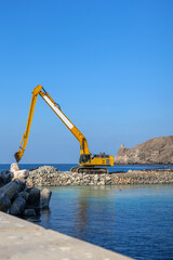 Fototapeta premium Marina development and waterfront infrastructure construction featuring excavator, stone embankment and marine engineering works