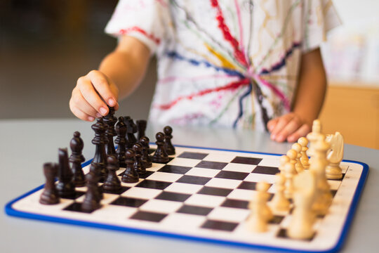 Close-up of a boy standing in front of a table picking up the king on a chessboard