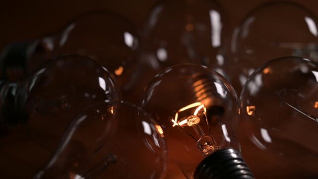 Glass incandescent light bulbs gradually lighting up on a dark background. Macro shot of electric lamps flashing with warm light symbolizing the birth of an idea and innovative thinking