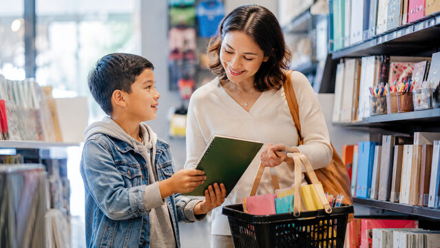 Smiling Mother and Young Son Shopping for Back to School Supplies, Choosing a Green Notebook in a Stationery Store Aisle