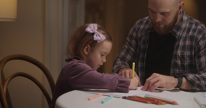 A father guides his daughter as they draw together, sharing joy and imagination in a warm, inviting room
