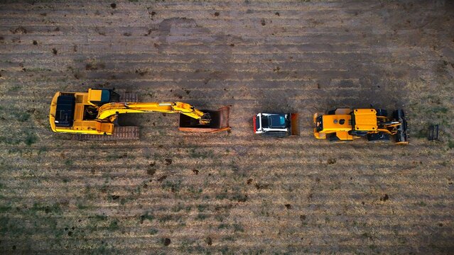 Aerial view of heavy construction machinery including an excavator, a skid steer, and a loader parked in a row on a tilled agricultural field in Loma, Colorado, United States.