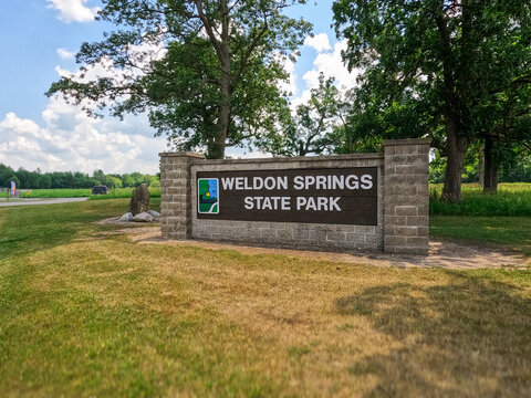 DeWitt County, Illinois, USA, July 4, 2025: Stone pillar entrance sign for Weldon Springs State Park with DNR logo, surrounded by summer greenery and trees under a cloudy sky.