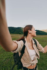 Fototapeta premium A woman with a backpack raises her arms in a bright outdoor field, smiling, embracing nature and freedom during a hiking adventure.