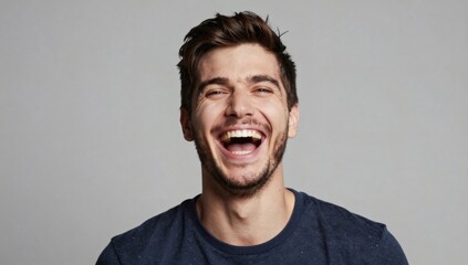Obraz premium Young man with brown hair laughs widely in a simple studio shot on gray